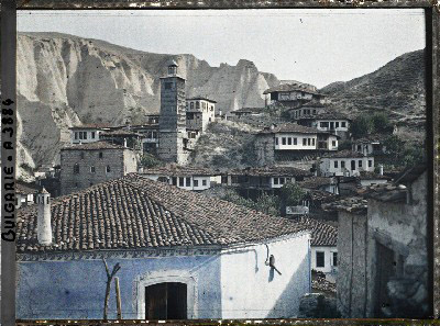 Maisons dont une, au premier plan, peinte en bleu, et tour de bois avec à l\'arrière-plan les falaises de grès. Melnik, Bulgarie, 18 septembre 1913.